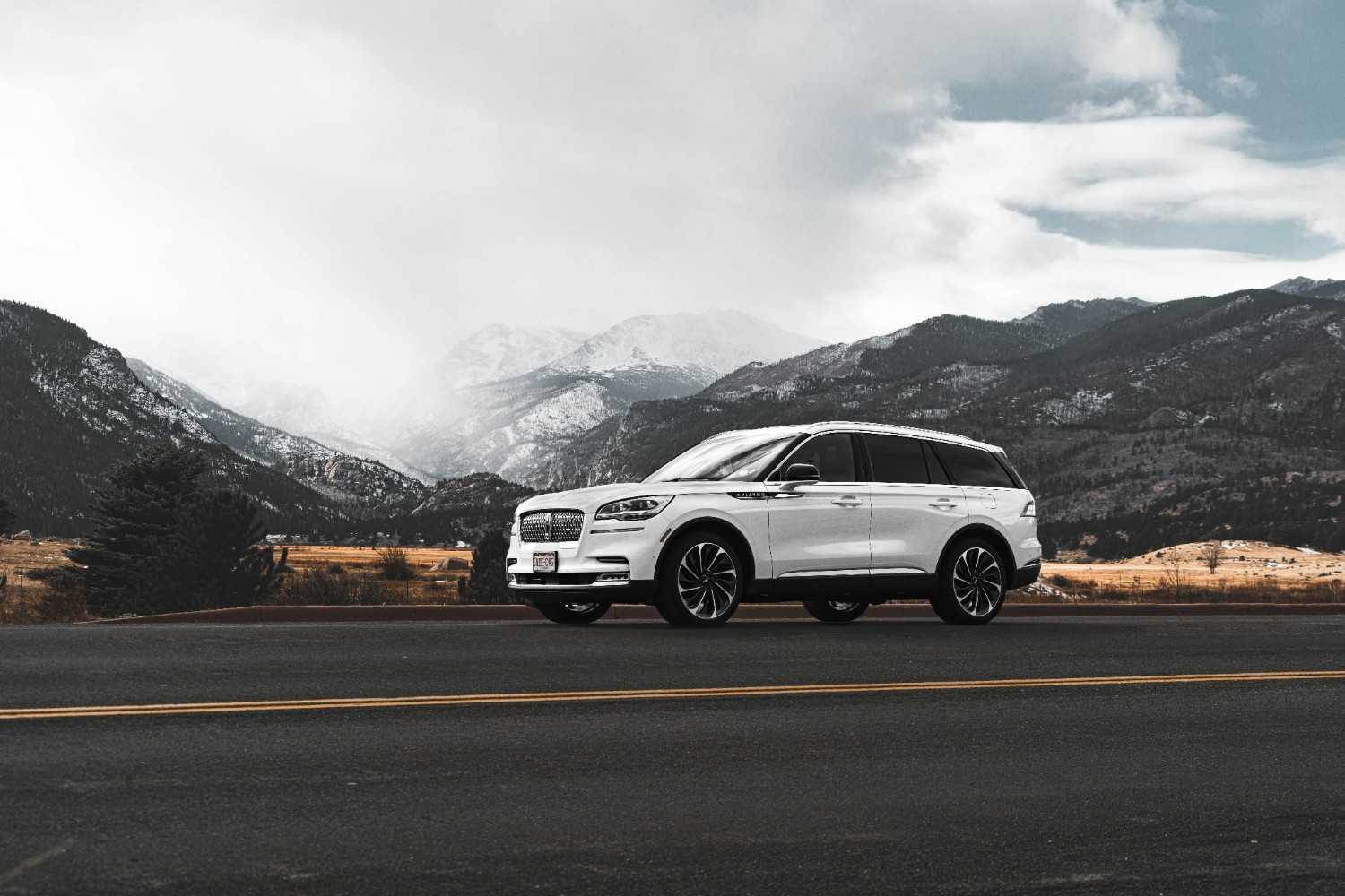A modern silver SUV driving on a clean open highway through a scenic mountain range
